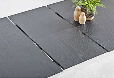 A dark charcoal gray wood-look rectangular table with three long panels folded out, shown in a clean studio-style setting with small decorative objects on top.