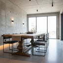 A rustic wooden dining table with a thick rectangular light oak top and dark brown trestle-style pedestal legs, photographed in a furniture showroom.