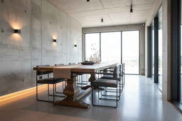 A rustic wooden dining table with a thick rectangular light oak top and dark brown trestle-style pedestal legs, photographed in a furniture showroom.