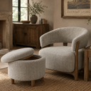 A light beige upholstered barrel chair with a curved back and wooden frame, paired with a matching round ottoman with a hinged lid in a warm, rustic living room setting.