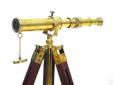 Handmade golden brass spyglass telescope resting on a handcrafted wooden tripod