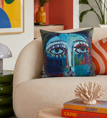 Teal abstract face velvet cushion styled on a sofa