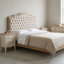 A light wood and tufted upholstered bed frame in a neutral beige bedroom setting, styled with white and beige linens, flanked by matching cream nightstands.
